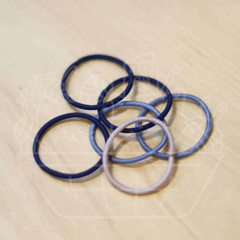 Blue hair elastics scattered on a light wooden surface on a beige table edge visible to the left.