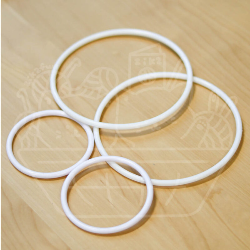 White plastic bangles of different sizes arranged on a light wooden surface.