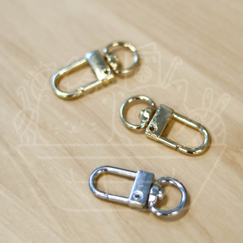Three small metal lobster-style clasps with attached key rings on a light wooden surface (gold and silver tones).