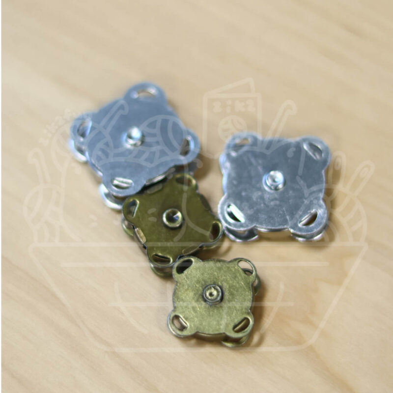 Metal square washer-like caps with four corner holes and a central rivet on a wooden surface.