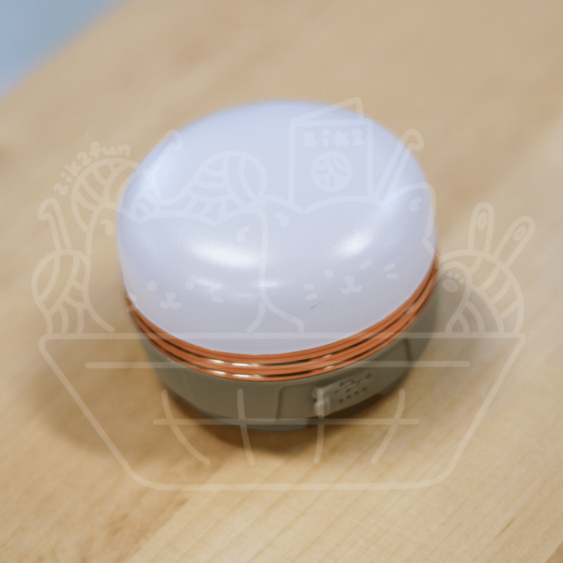 Round white lid with a cute cat illustration atop a small gray base with a copper-colored ring, placed on a wooden table.
